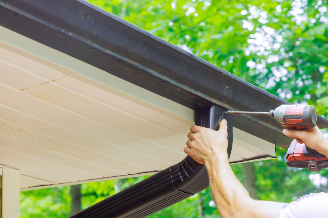 Installer drilling a downspout in place.